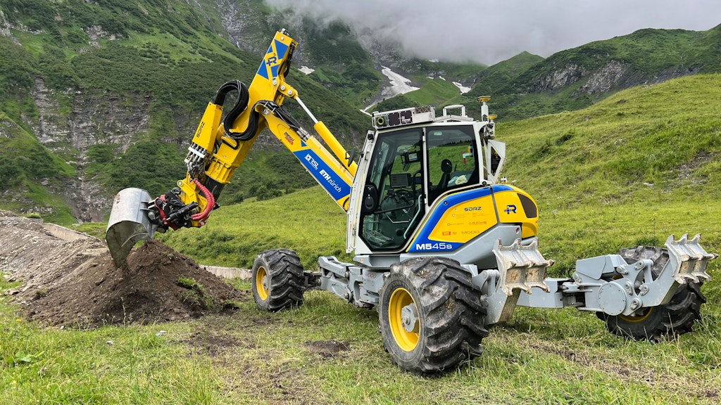 An unmanned, yellow excavator, which is operated by remote control and is in the process of dig-ging a trench. Nature can be seen in the background. 