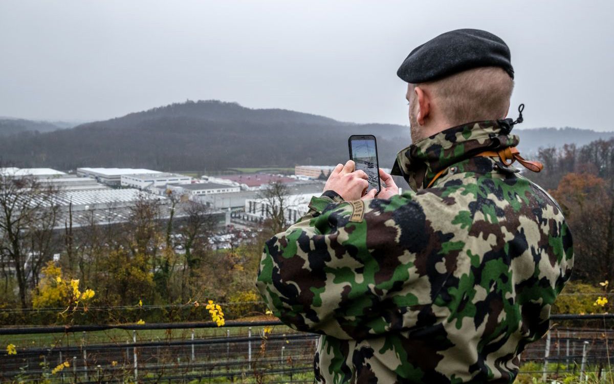 A soldier in uniform uses his smartphone in the training area.