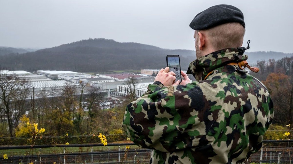 A soldier in uniform uses his smartphone in the training area.