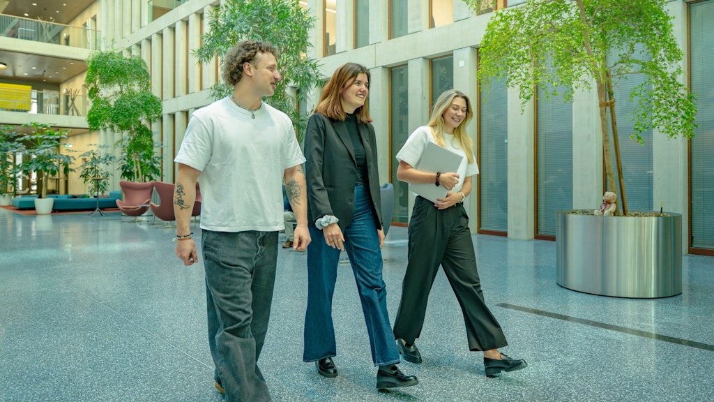 3 Hochschulabsolventen/-innen laufen durch das Atrium.