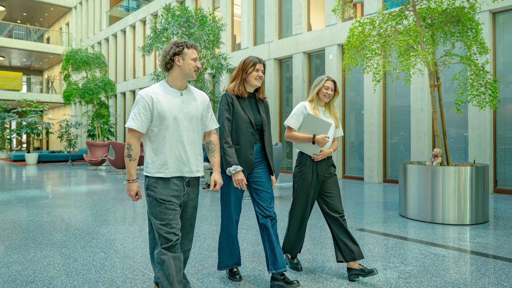 Trois diplômé·e·s universitaires traversent l’atrium.