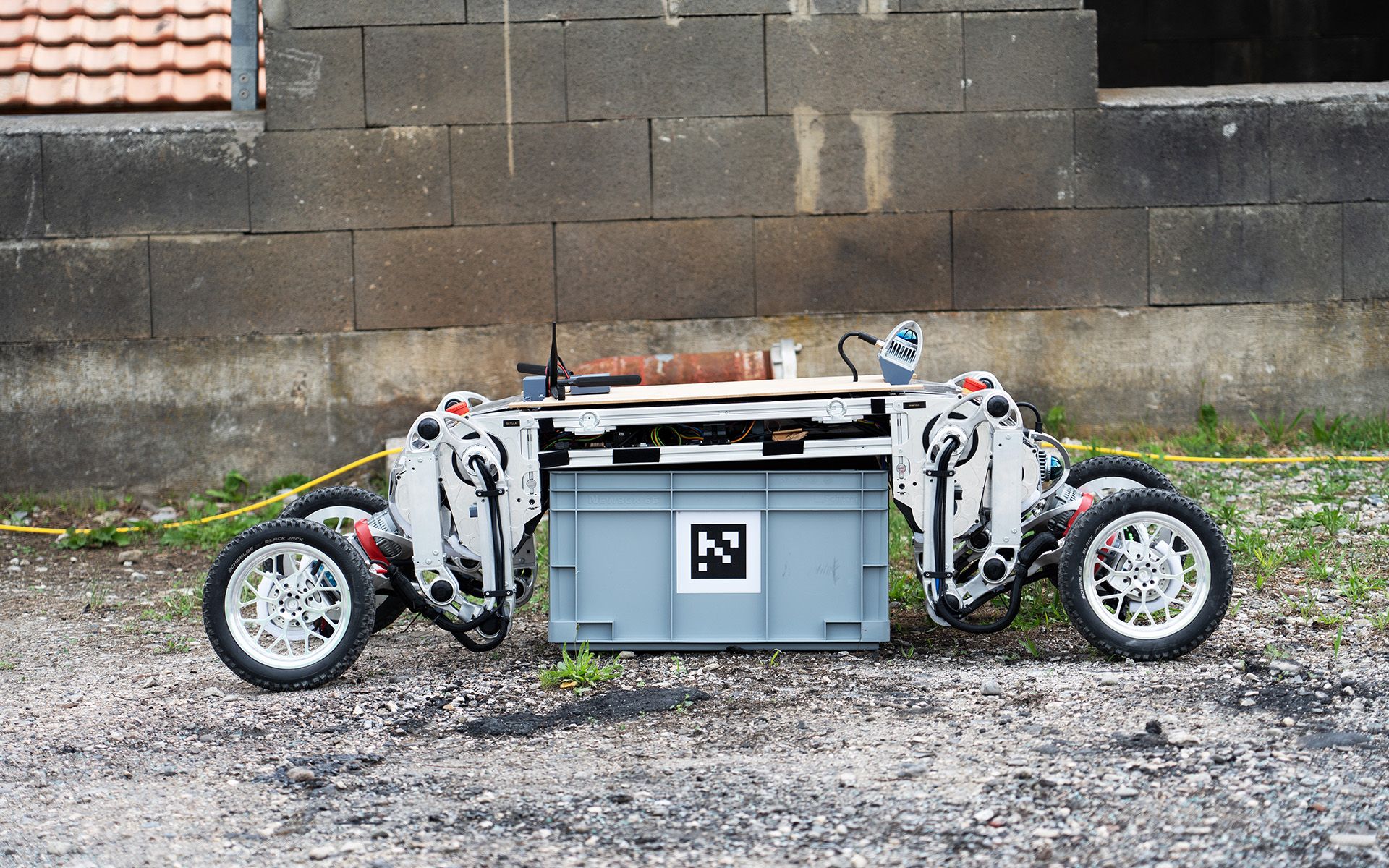 Ein Roboter mit vier Rädern greift sich eine graue Kiste.