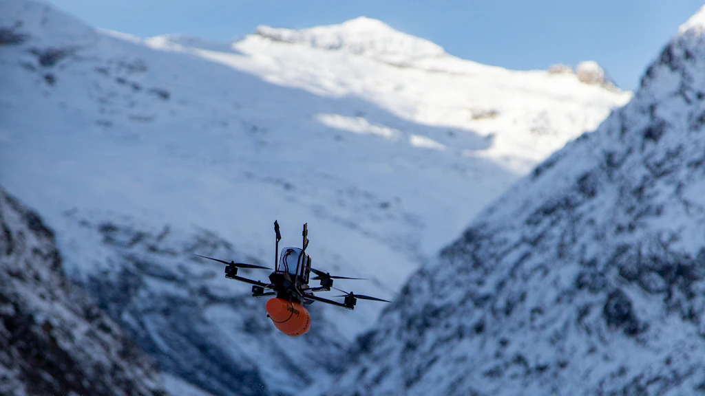 Drohne fliegt an verschneiten Bergen vorbei.
