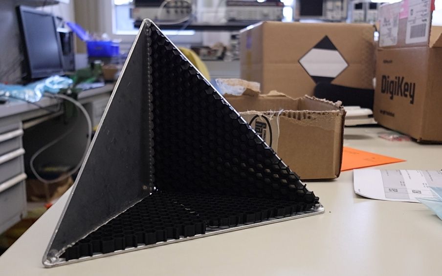 Dreieckige schwarze Module, mit Löcher, befinden sich in einem pyramiden-förmigen Behältnis.