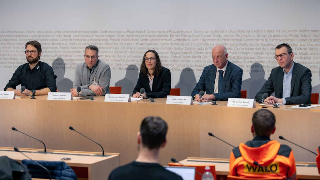 Auf dem Podium des grossen Konferenzsaales sitzen die Gewinner, die Projektleitung von armasuisse W+T sowie der Mediensprecher.