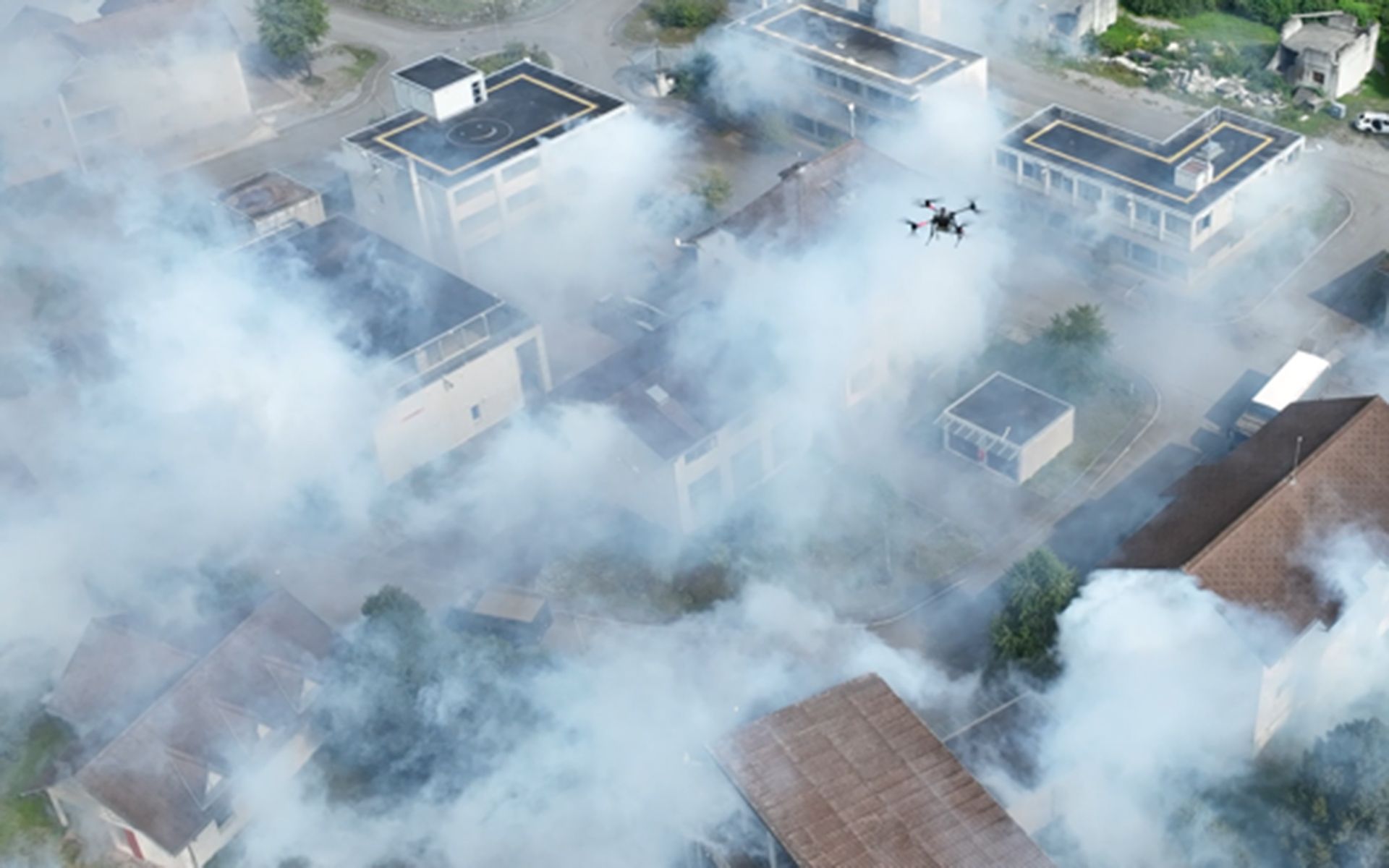 Drohne fliegt über ein im Rauch liegendes Dorf.