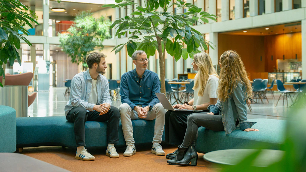 Vier Personen sitzen im Atrium und halten eine Besprechung.