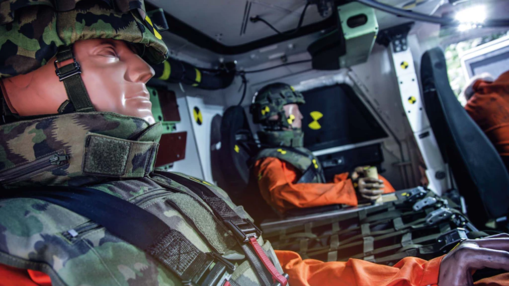 The models are seated in an armored vehicle with protective equipment.