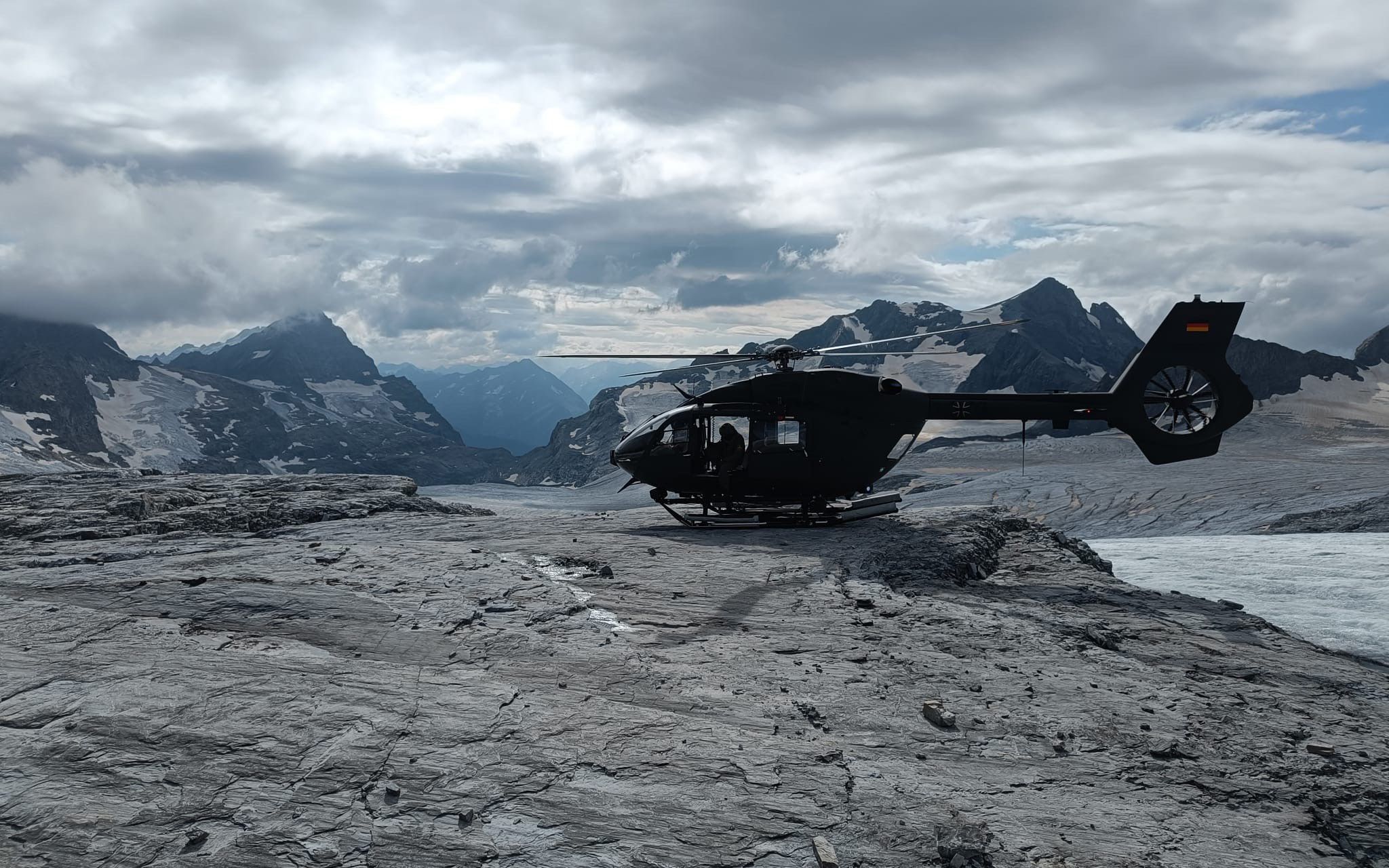 A helicopter situated on rocks in front of a glacier.  