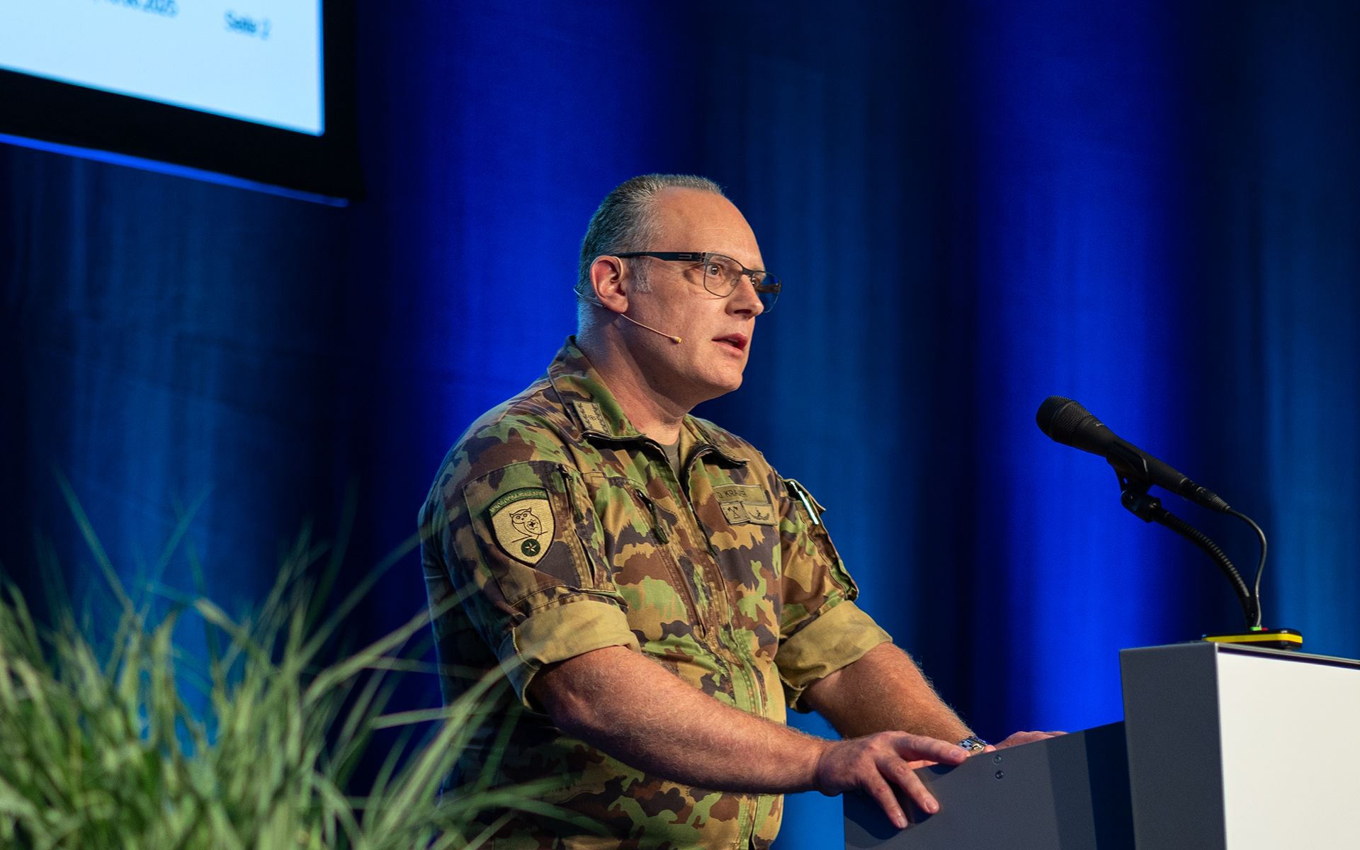 A person is giving a presentation at a lectern in front of a large audience.