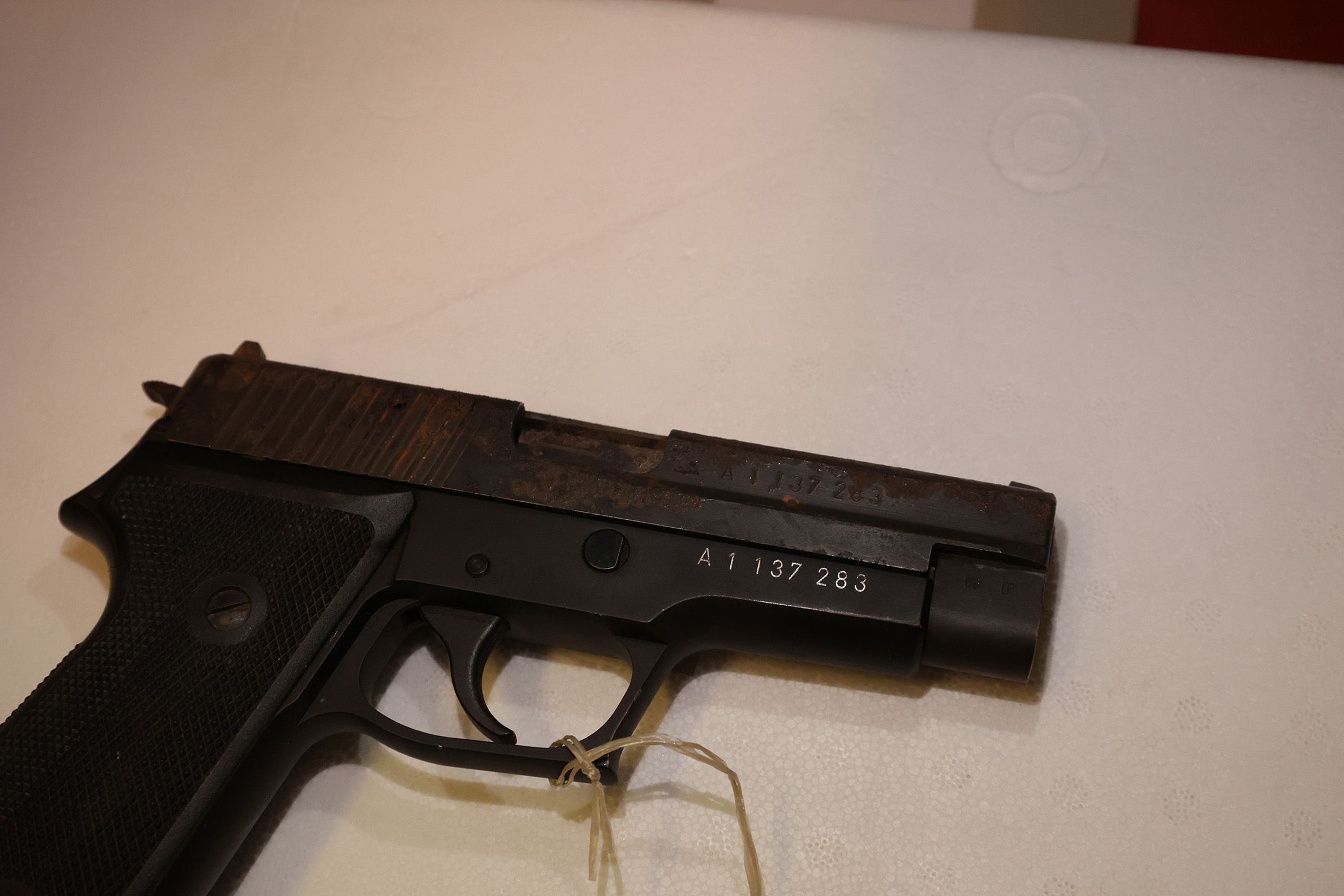 A pistol is on the table. We can see the weapon serial number embedded in colour.