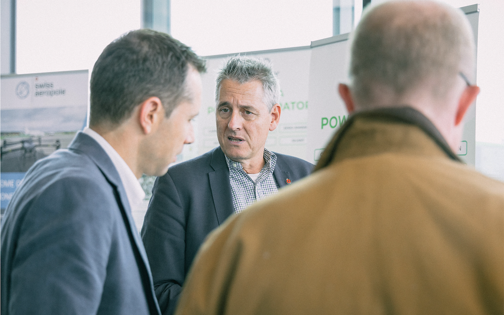 Three men standing side by side in front of posters
