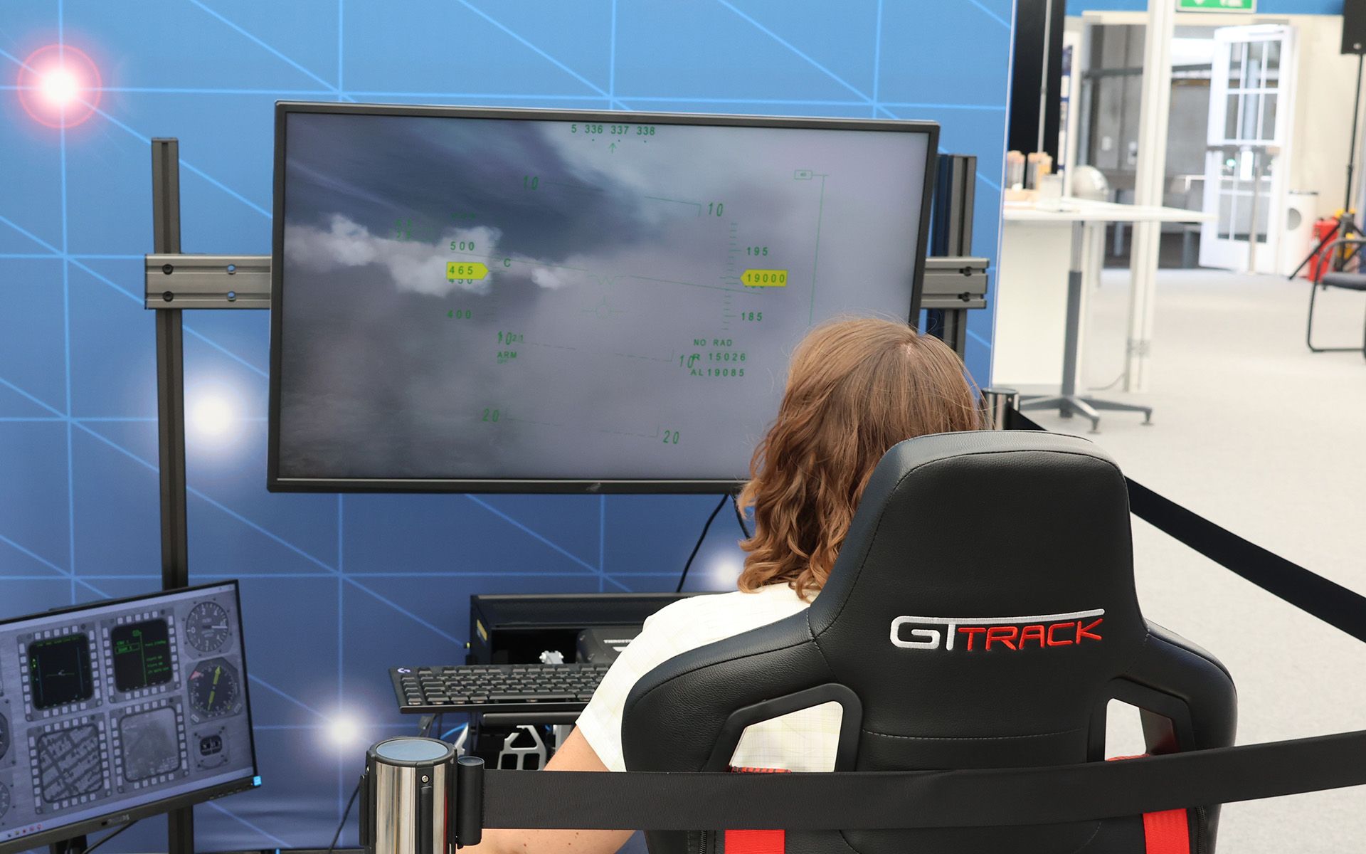 We see a woman from behind in front of a flight simulator. 