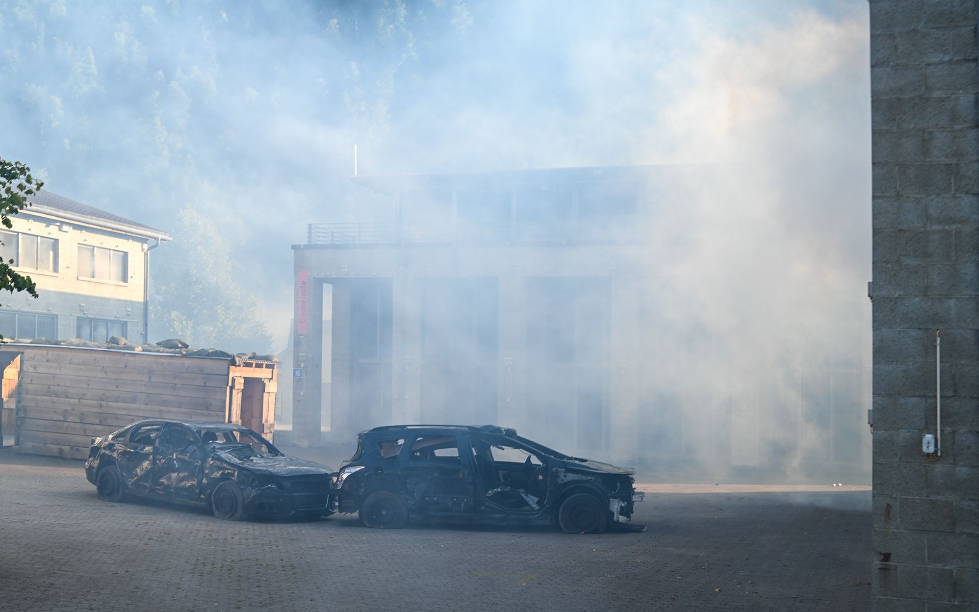 Two destroyed cars between buildings surrounded by fog. 