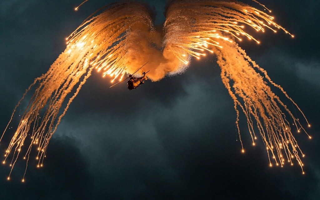 A helicopter flies through the night and fires flares.