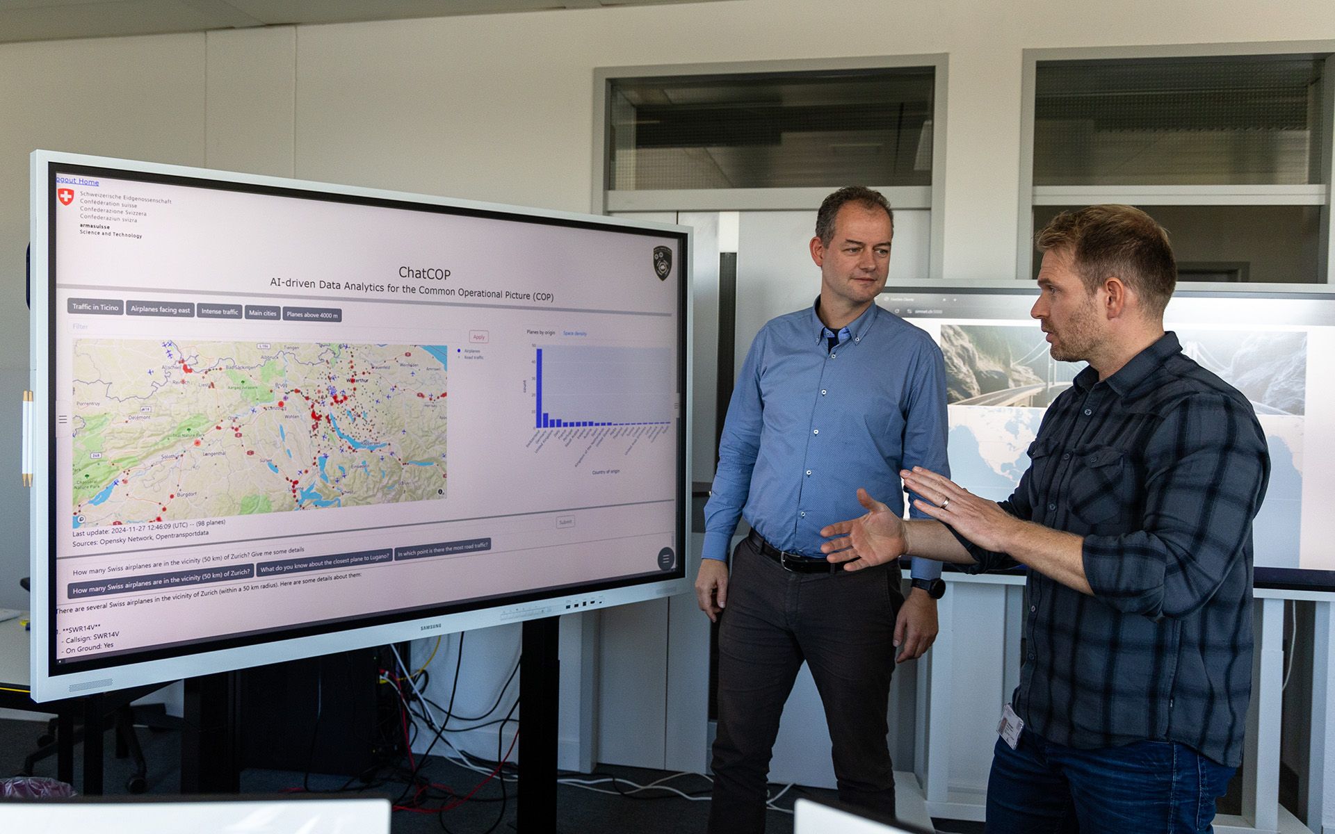 Dr Michael Rüegsegger and Adrian Christ standing in front of a large screen in the SimLab.