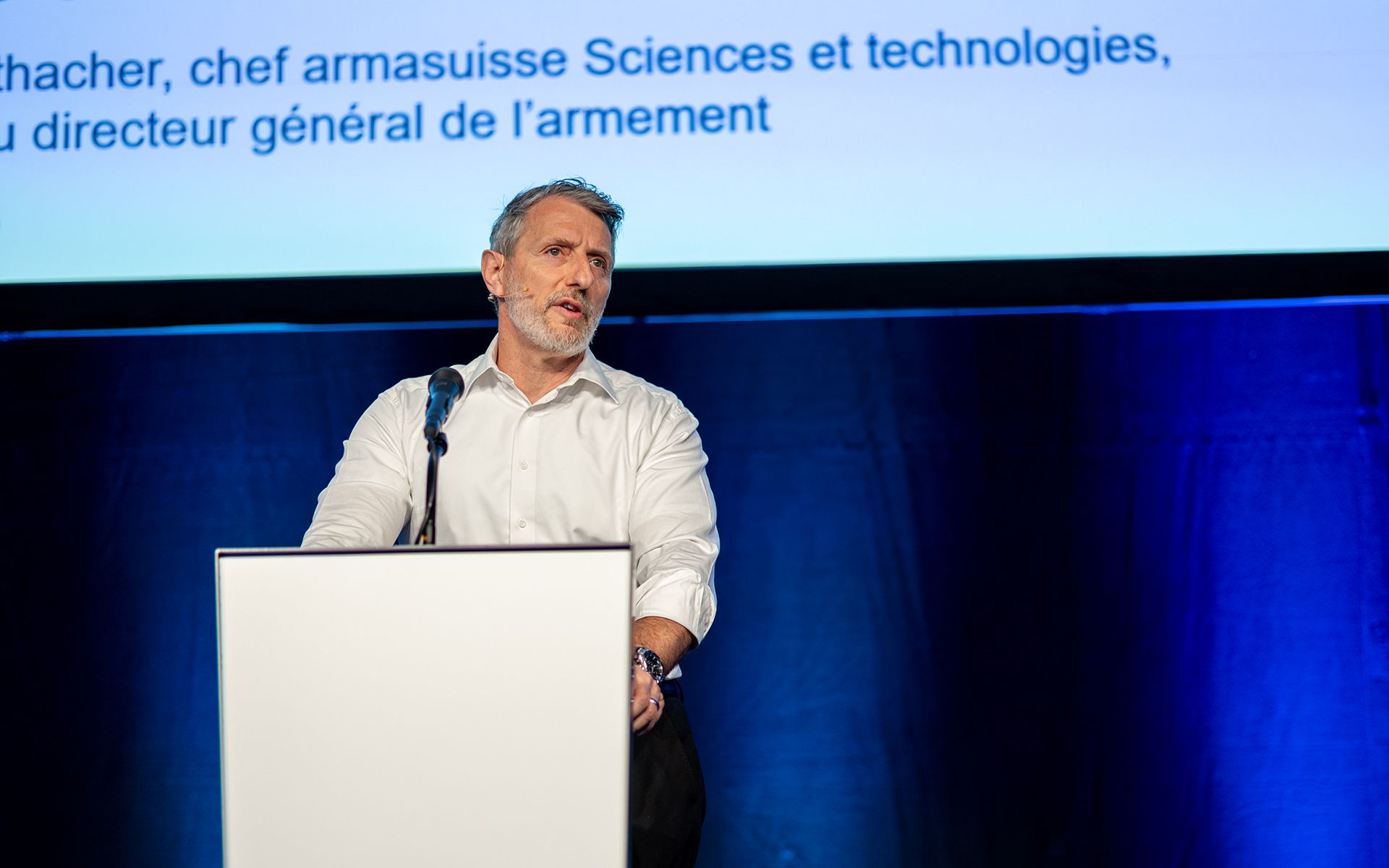 A person is giving a presentation at a lectern in front of a large audience.