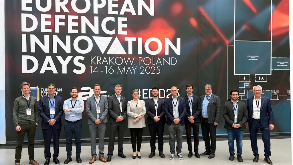 People are standing in front of a wall bearing the words “European Defence Innovation Days, Krakow, Poland”.