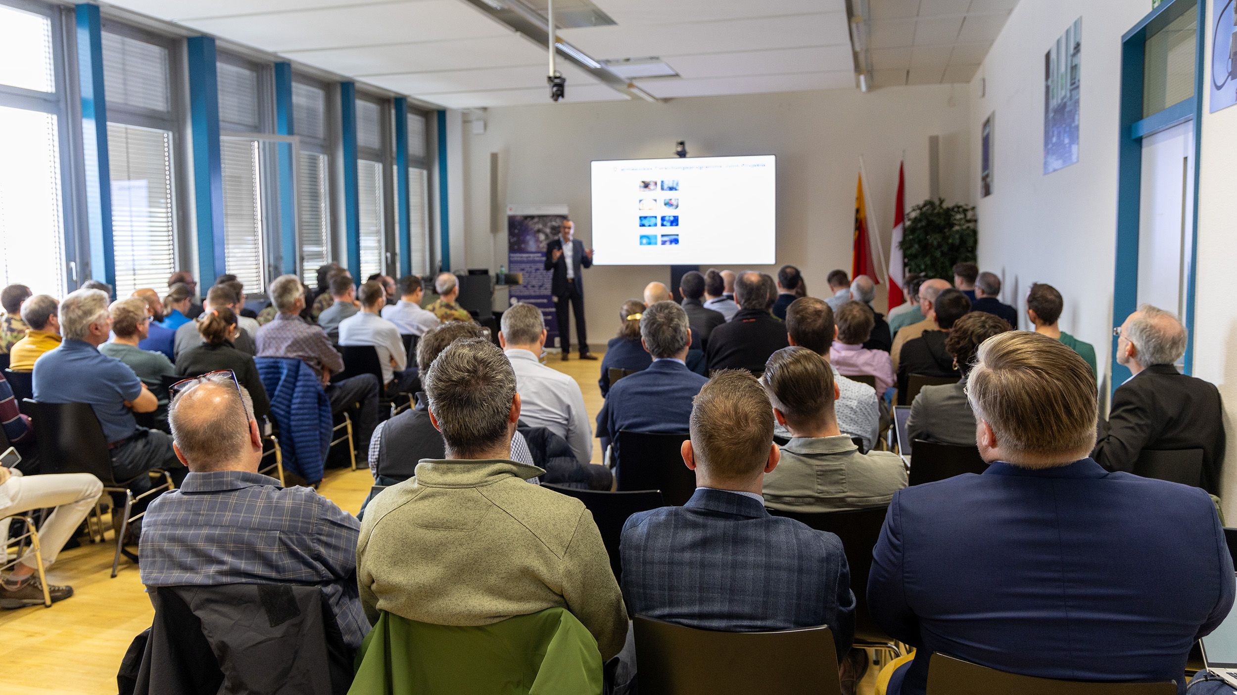 Peter Wellig parle à un public assis. Il donne sa présentation devant plusieurs rangées d’auditoire.