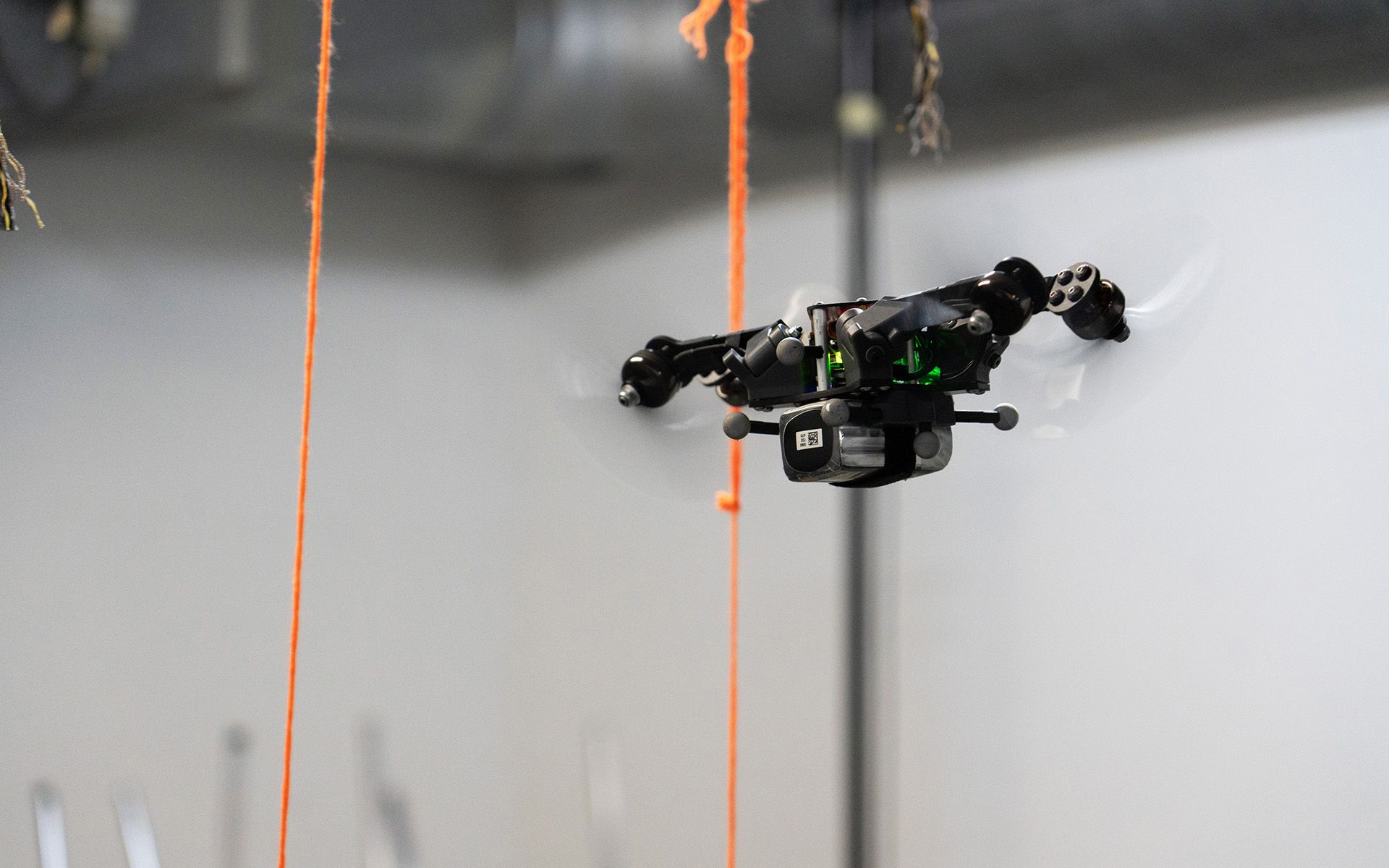 Un drone avec ses bras repliés vole entre deux fils orange. 