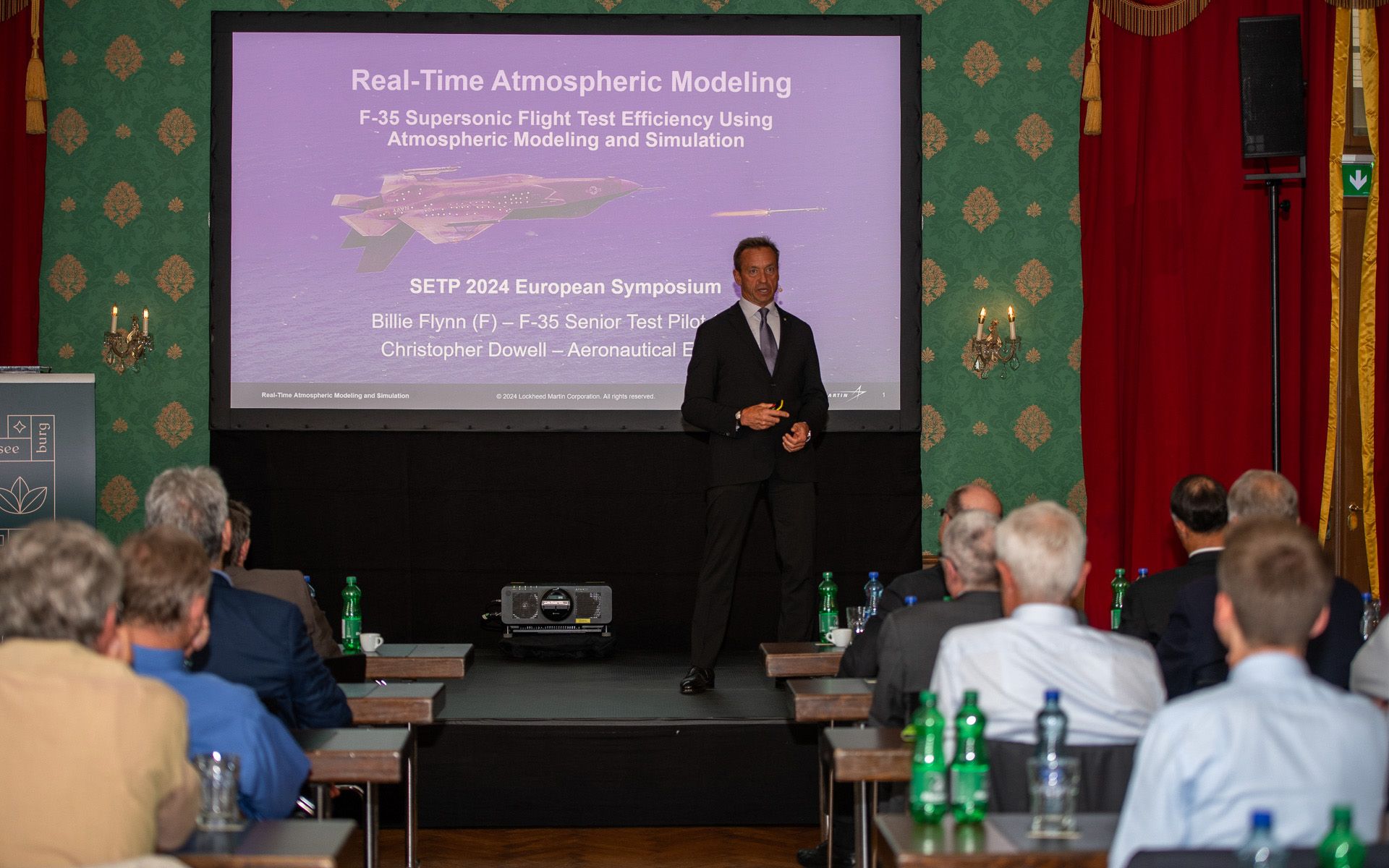 Un homme en costume noir est en train de faire un exposé sur scène.