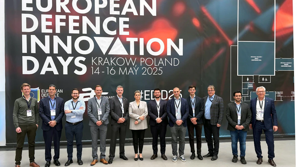 Des personnes se tiennent devant un mur sur lequel est écrit « European Defence Innovation Days, Krakow, Poland ». 