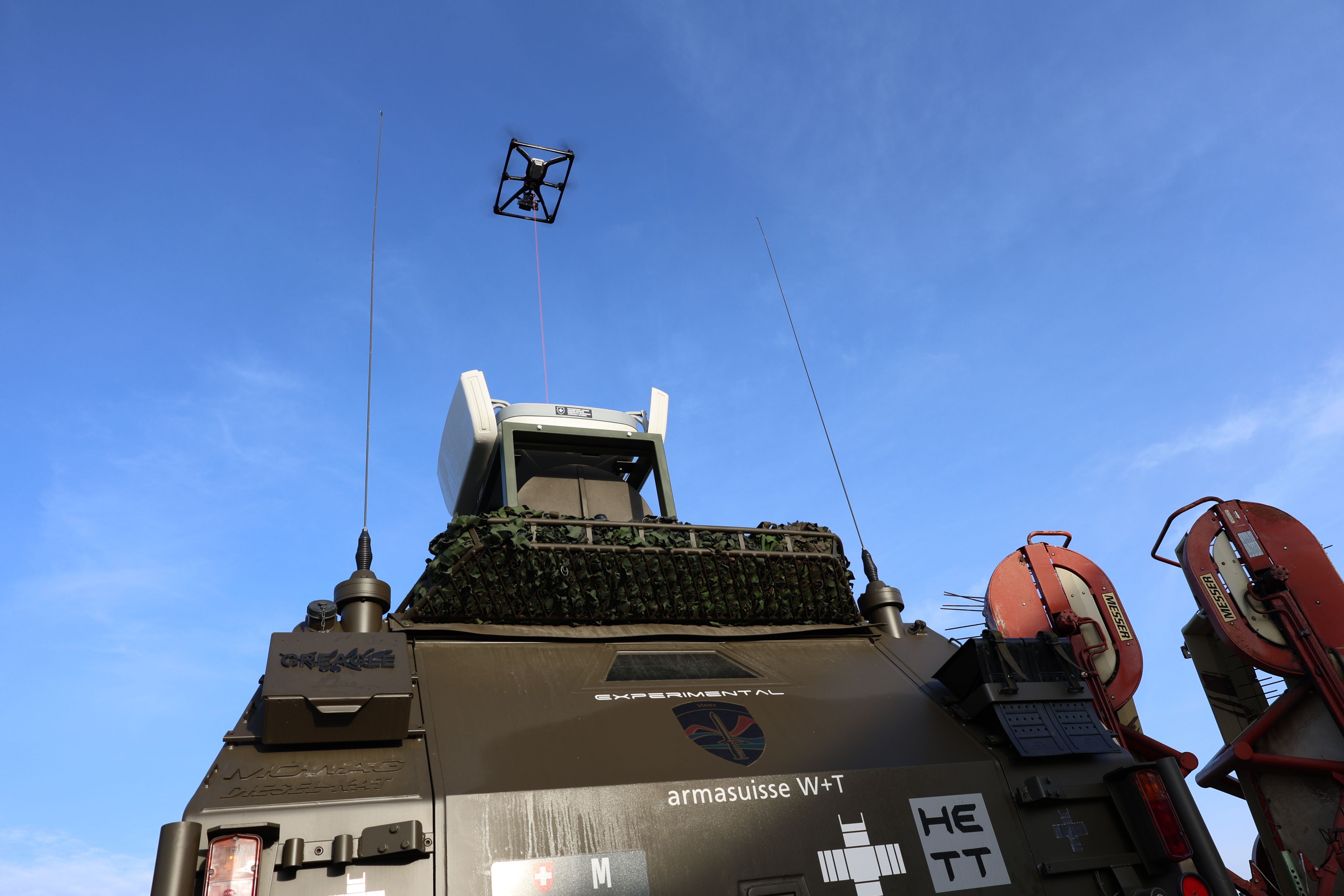 Le drone d'un véhicule militaire vole en l'air au bout d'une corde.