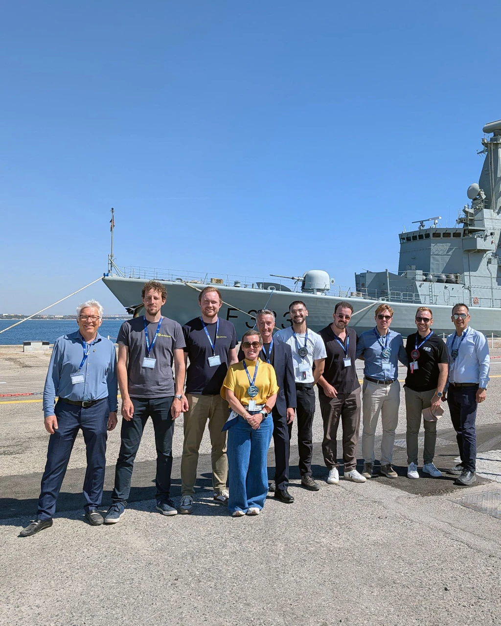 I rappresentanti della delegazione svizzera al REPMUS 2026 posano per una foto di gruppo davanti a una nave della Marina.