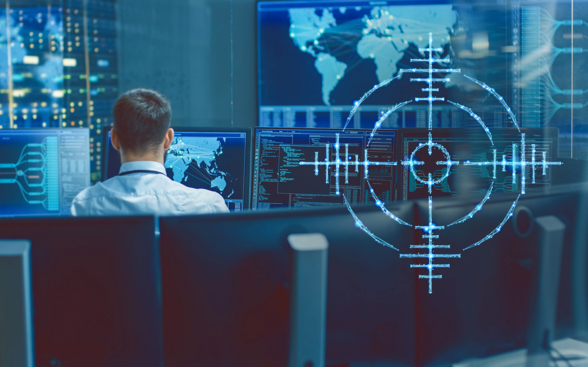 In primo piano si vede una croce di bersaglio. Sullo sfondo una persona seduta al computer.