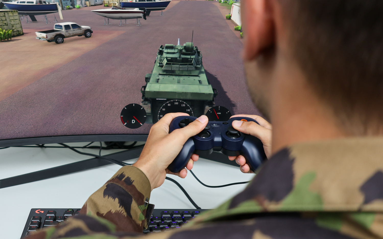 Un uomo in tuta mimetica tiene in mano un controller Playstation e gioca a un gioco di simulazione