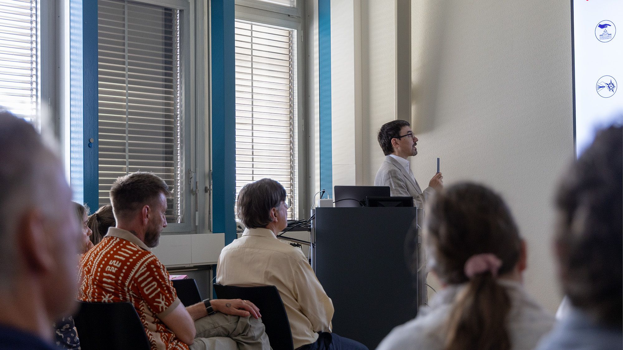 In piedi dietro a un leggio, con uno schermo al suo fianco, il dott. Ronny Lorenzo presenta al pubblico il programma di ricerca 4 «Efficacia bellica, protezione e sicurezza».