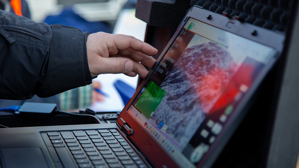 Una mano indica una mappa digitale del terreno montuoso sullo schermo di un computer portatile.