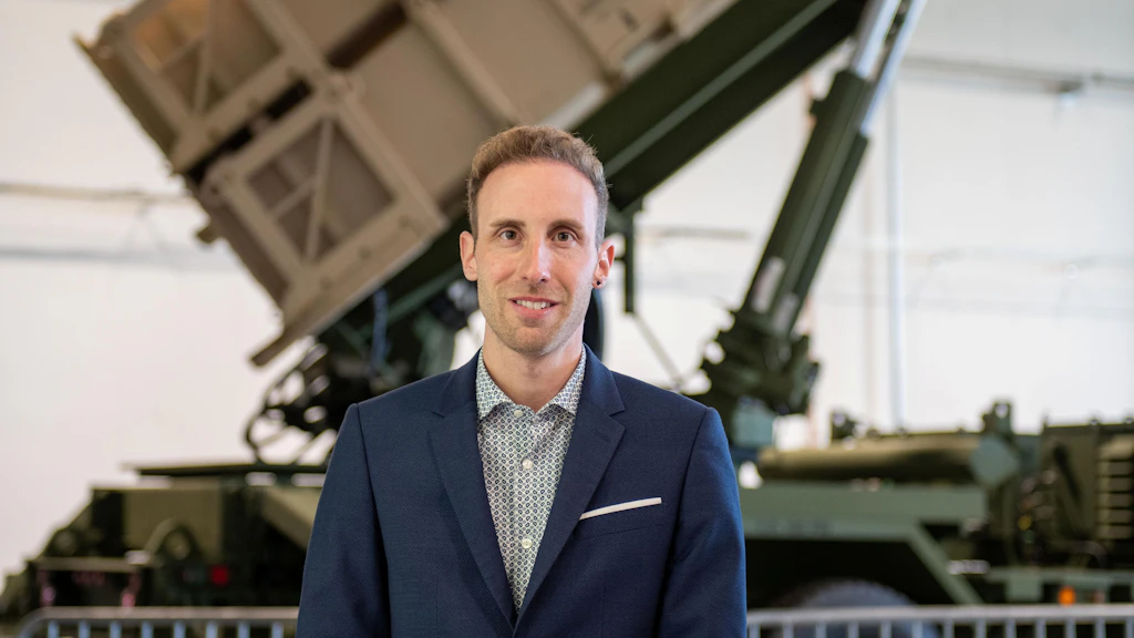 Un uomo in abito blu è in piedi davanti a un veicolo militare