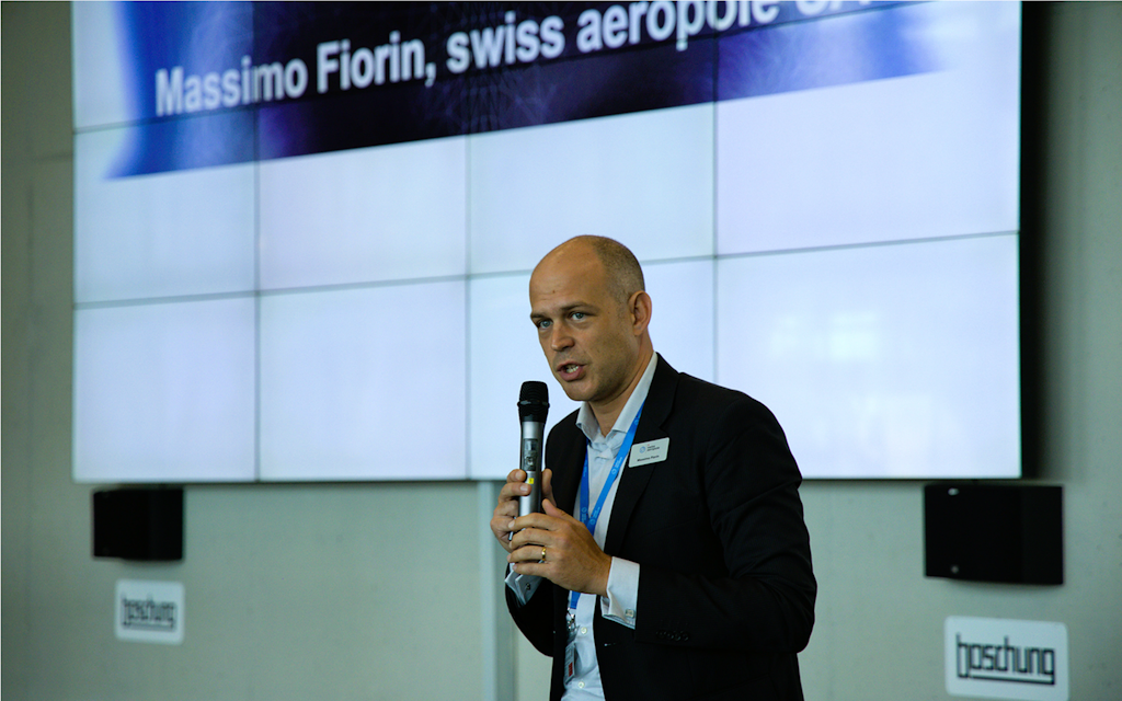 Un uomo in abito elegante con un microfono in mano davanti a uno schermo