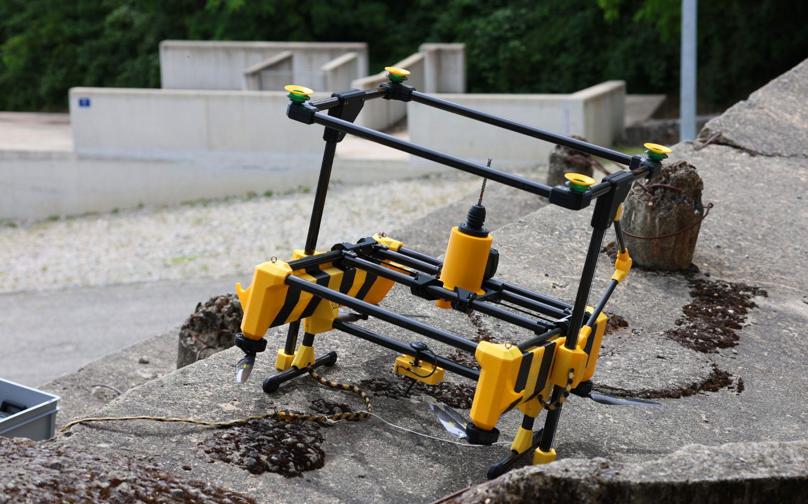 Un drone a strisce gialle e nere e un trapano a terra. 