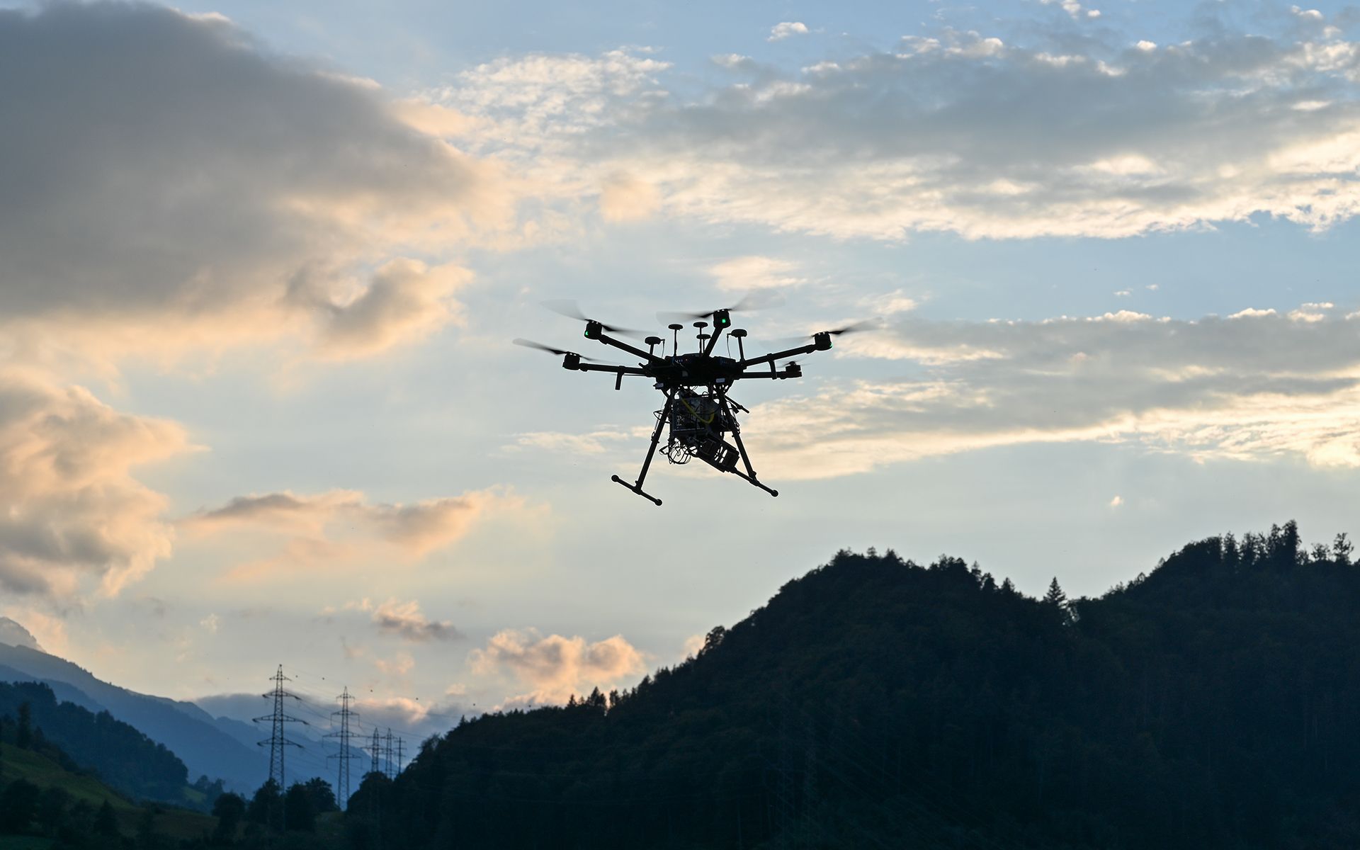 Un drone in volo nel cielo al tramonto, con nuvole e il paesaggio sullo sfondo.